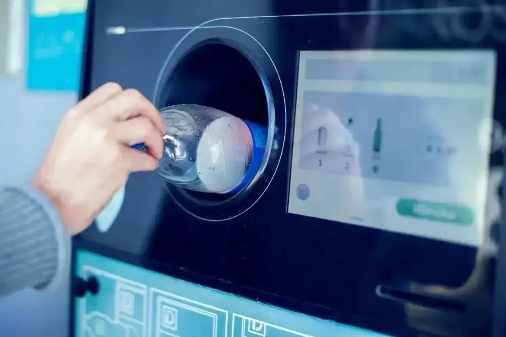 Hand placing empty plastic bottle into bottle deposit machine